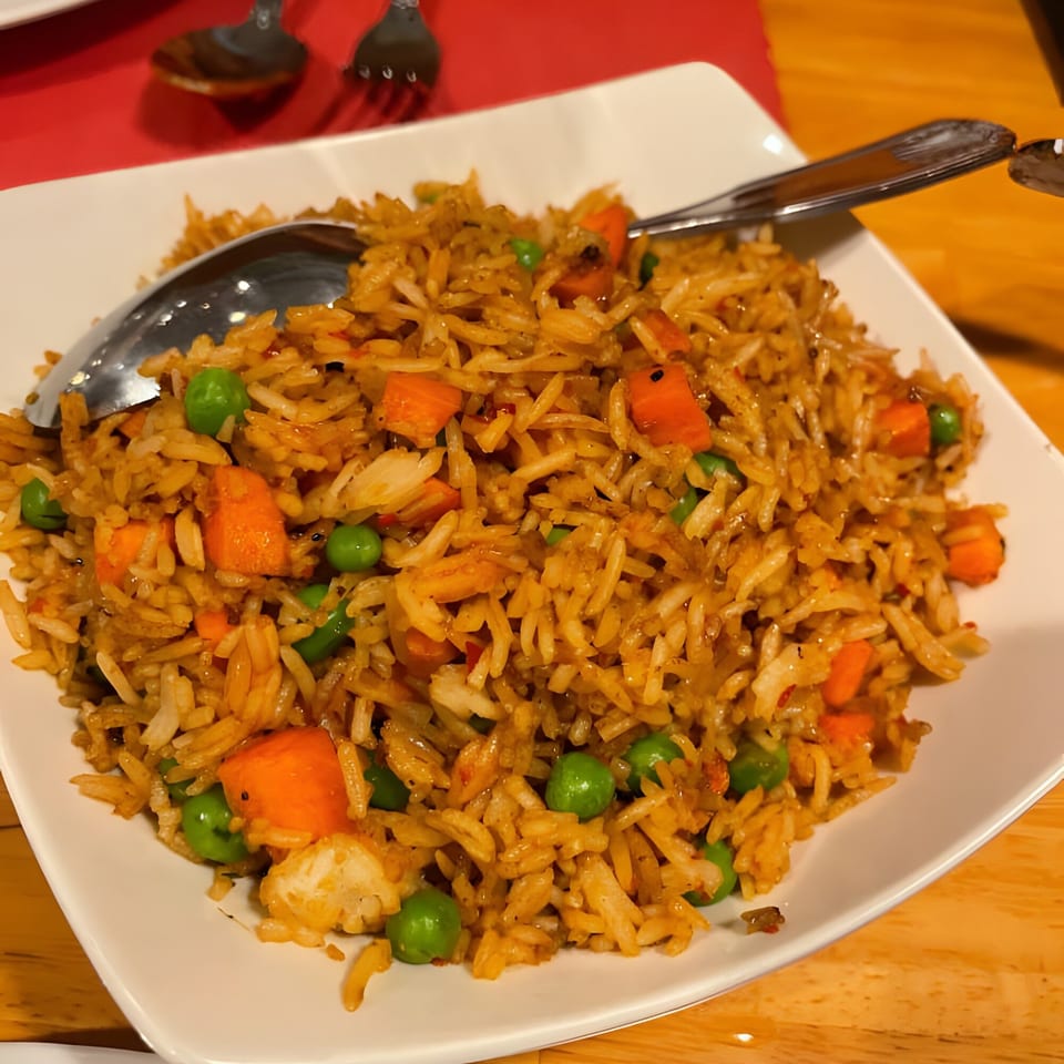 A white rectangular plate filled with Indian fried rice, carrots, and green peas, with a spoon.