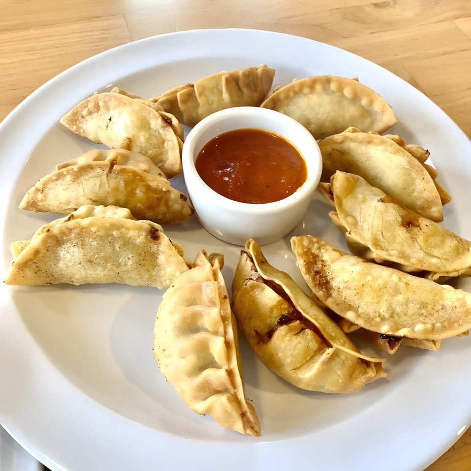 A white plate with fried momos arranged around a small bowl of red dipping sauce.